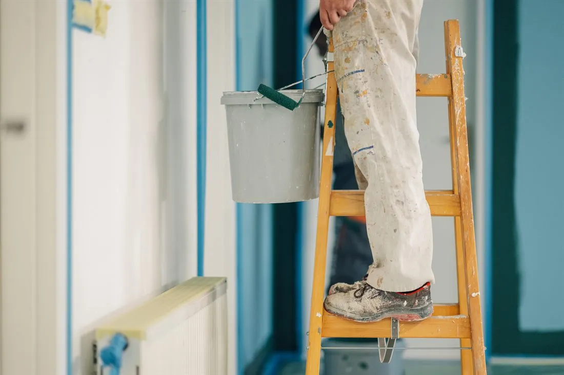 Imbianchino al lavoro su una scala con secchio di vernice